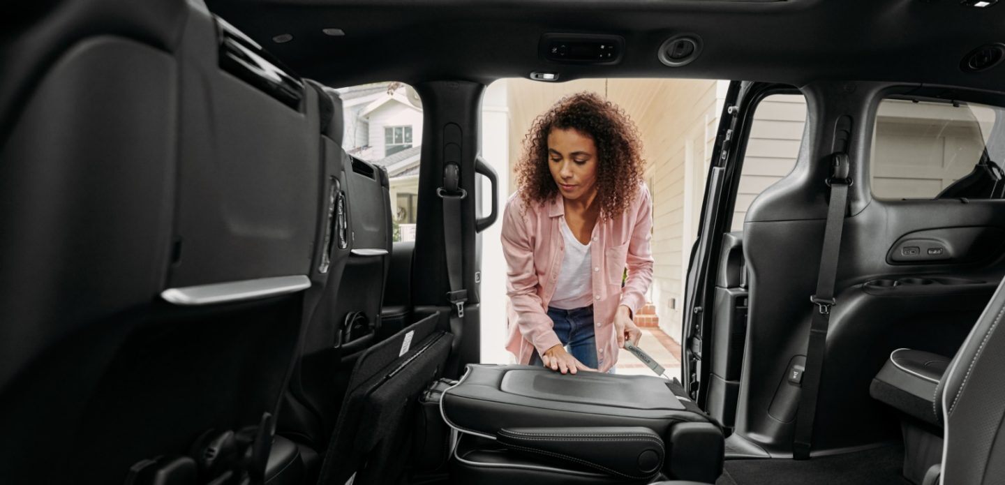 Se muestra: Una mujer de pie junto a la puerta deslizable lateral abierta en la Chrysler Pacifica Limited 2023 con el paquete de apariencia S, plegando el respaldo del asiento del lado del pasajero de la segunda fila.