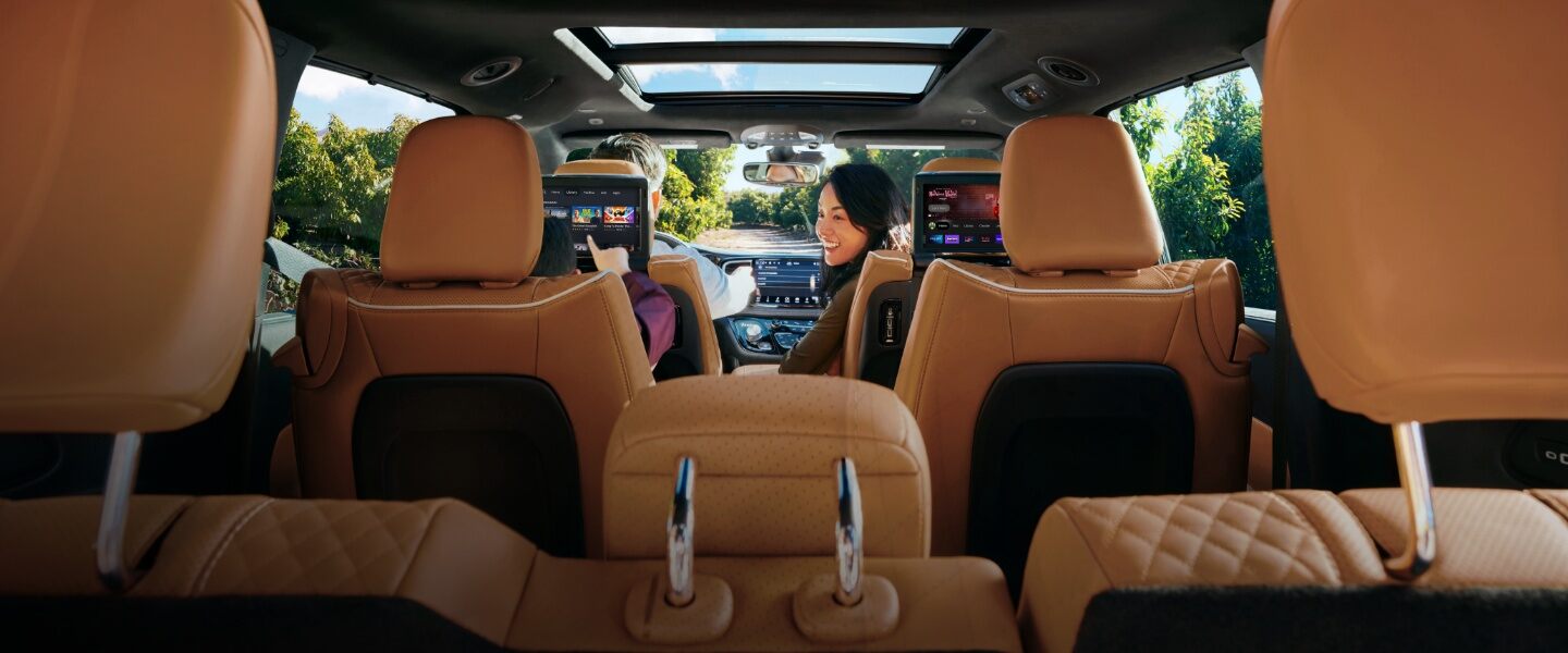 El interior de la Chrysler Pacifica Pinnacle 2023 con un hombre conduciendo y una mujer mirando hacia atrás a un niño en la segunda fila que está jugando en la pantalla táctil instalada en el respaldo del asiento.