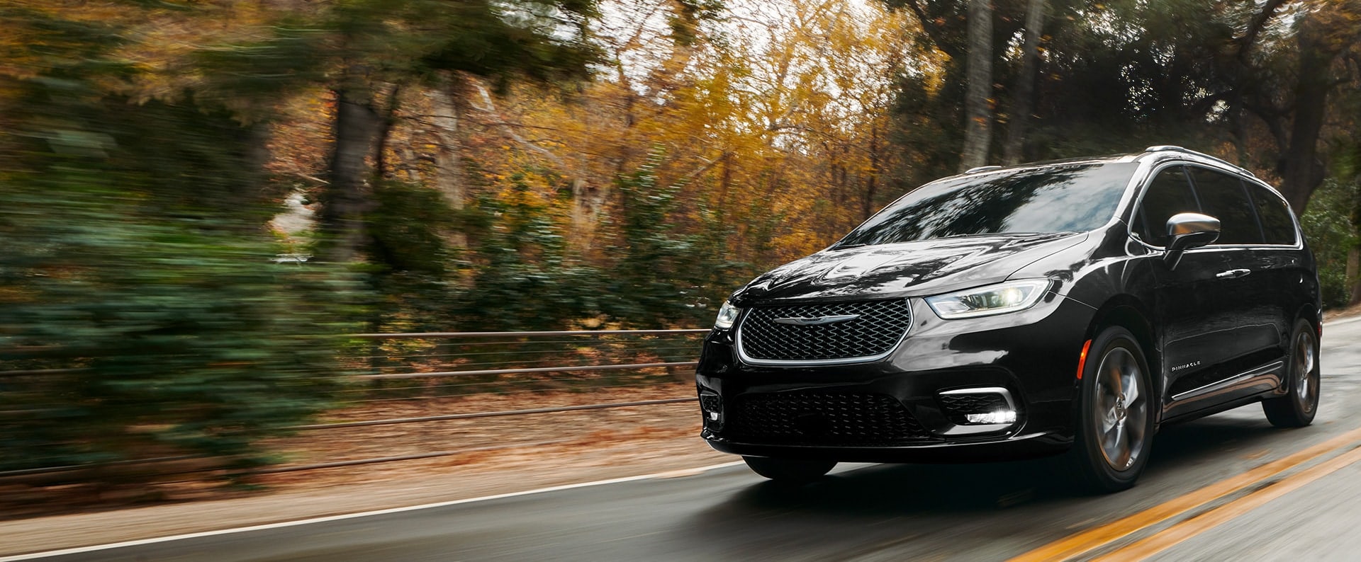 Perfil desde el ángulo del conductor de la Chrysler Pacifica Pinnacle 2024 circulando por un camino campestre; el fondo está borroso para indicar que el vehículo está en movimiento.