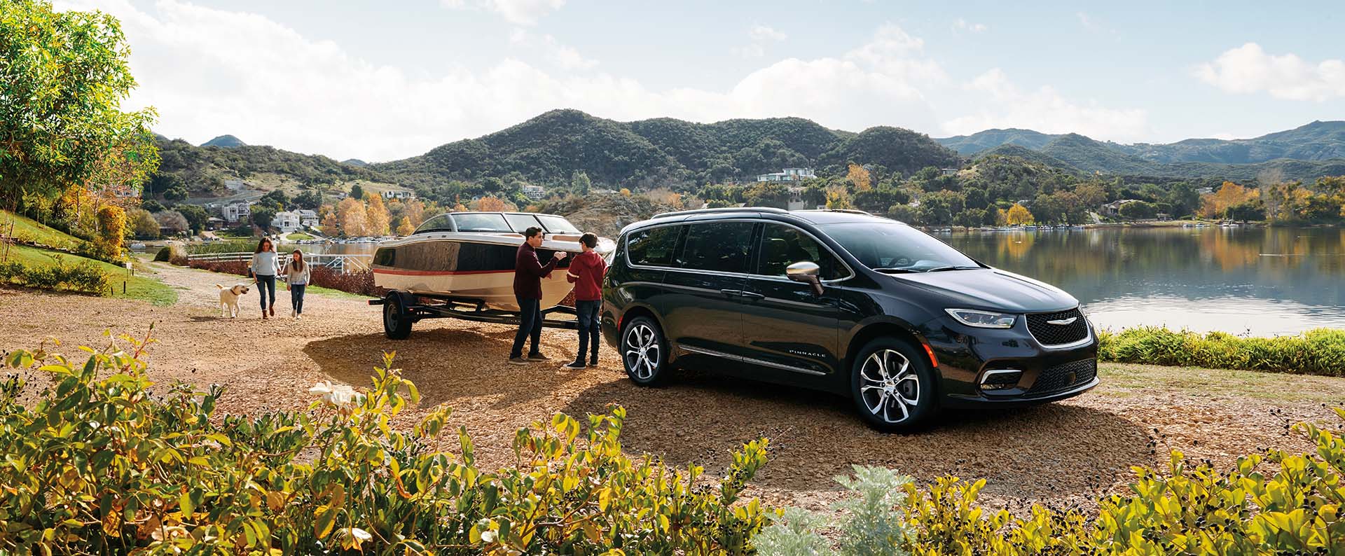 Una Chrysler Pacifica Pinnacle 2024 estacionada junto a un lago, con una lancha remolcada y una familia de cuatro miembros cerca.