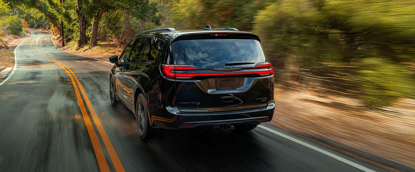 Perfil trasero del lado del conductor de la Chrysler Pacifica Pinnacle 2025 circulando por un camino campestre; el fondo está borroso para indicar que el vehículo está en movimiento.