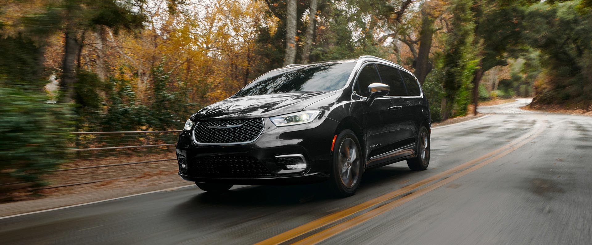 Perfil desde el ángulo del conductor de la Chrysler Pacifica Pinnacle 2025 circulando por un camino campestre; el fondo está borroso para indicar que el vehículo está en movimiento.