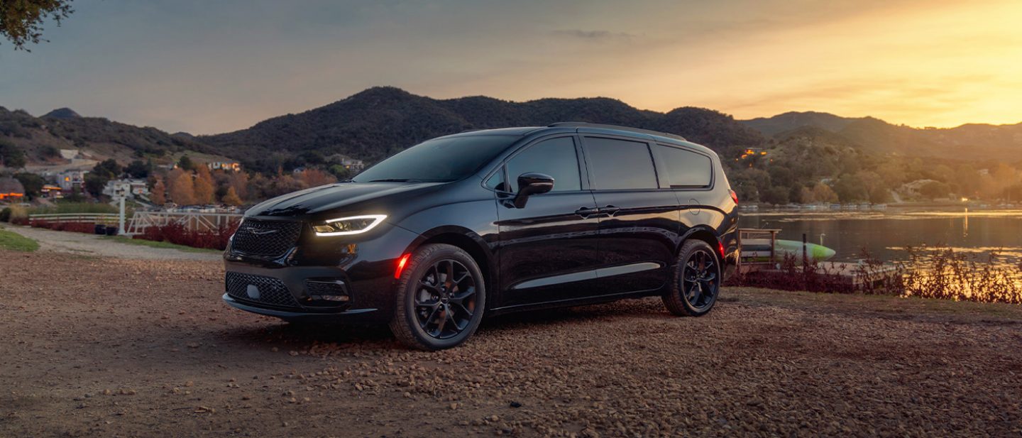 Imagen Una Chrysler Pacifica Limited 2025 negra estacionada al lado de un lago, al atardecer.