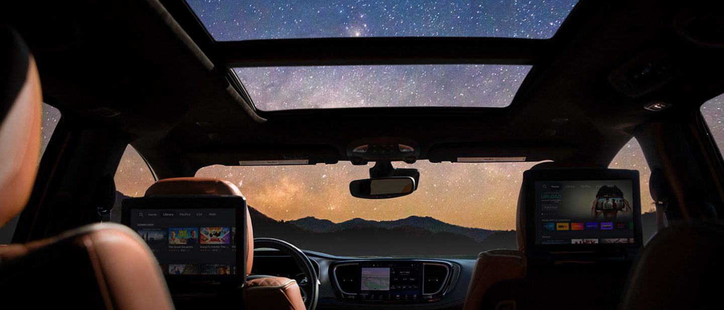 Imagen El techo corredizo de doble panel de la Chrysler Pacifica Pinnacle 2025 está abierto para revelar el cielo nocturno repleto de estrellas, mientras que las dos pantallas táctiles instaladas en la parte trasera de los asientos muestran una variedad de selecciones.