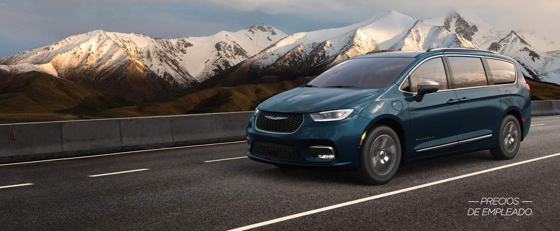 Una Chrysler Pacifica Pinnacle Plug-In Hybrid 2025 azul circulando por una autopista, con montañas de fondo. Evento de ventas Precios de empleado.