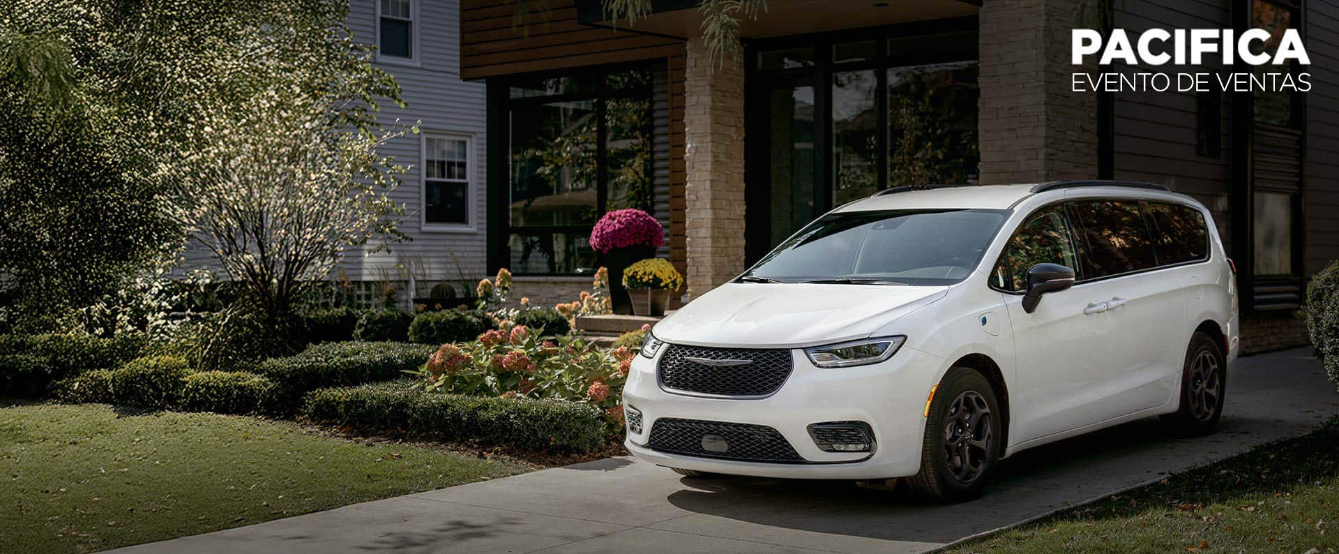 Ángulo delantero del lado del conductor de una Chrysler Pacifica Select Plug-in Hybrid 2025 blanca con el paquete apariencia Premium S, estacionada en la entrada de una casa en un vecindario. Evento de ventas de Chrysler Pacifica.