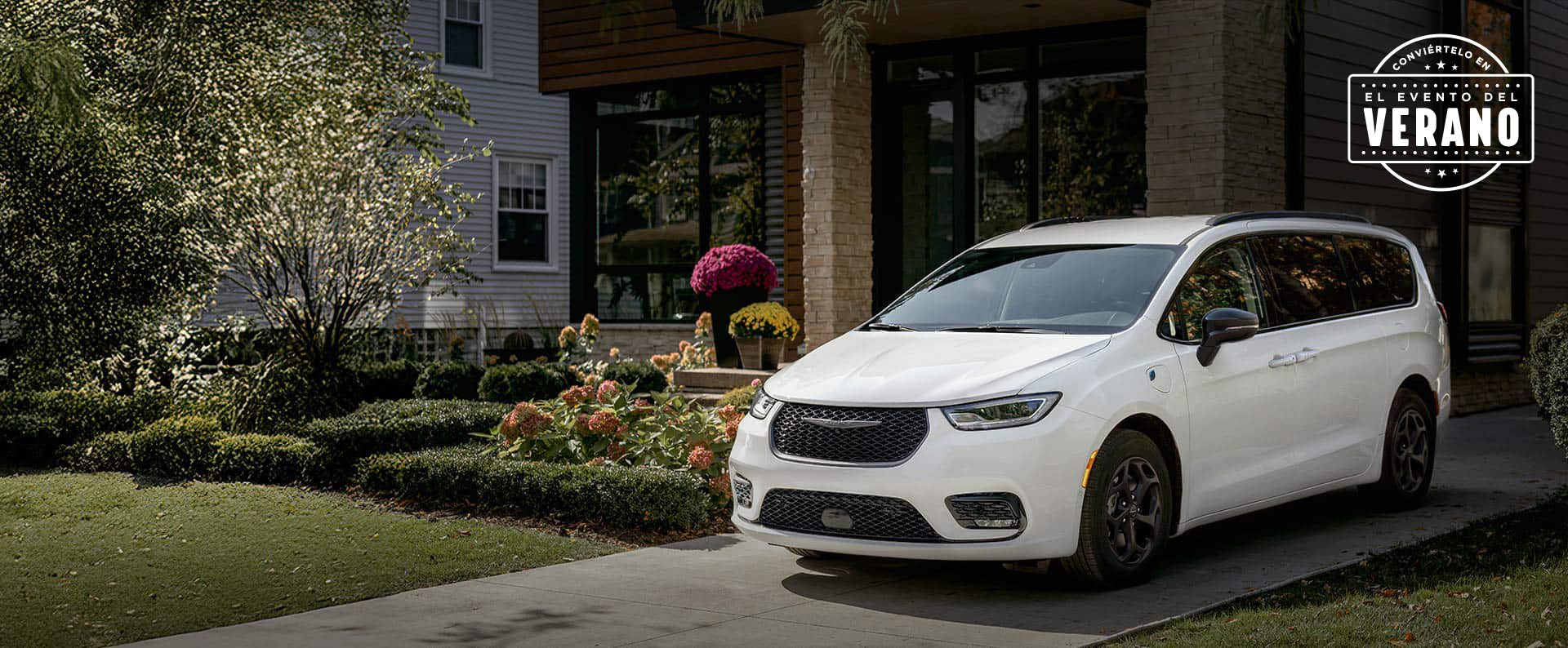 Ángulo delantero del lado del conductor de una Chrysler Pacifica Select Plug-in Hybrid 2025 blanca con el paquete apariencia Premium S, estacionada en la entrada de una casa en un vecindario. Conviértelo en el evento de ventas del verano​​​​​​​.
