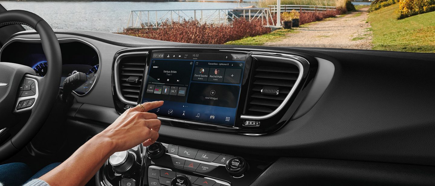 Mostrar Una conductora en una Chrysler Voyager LX 2025 seleccionando música en la pantalla táctil Uconnect.