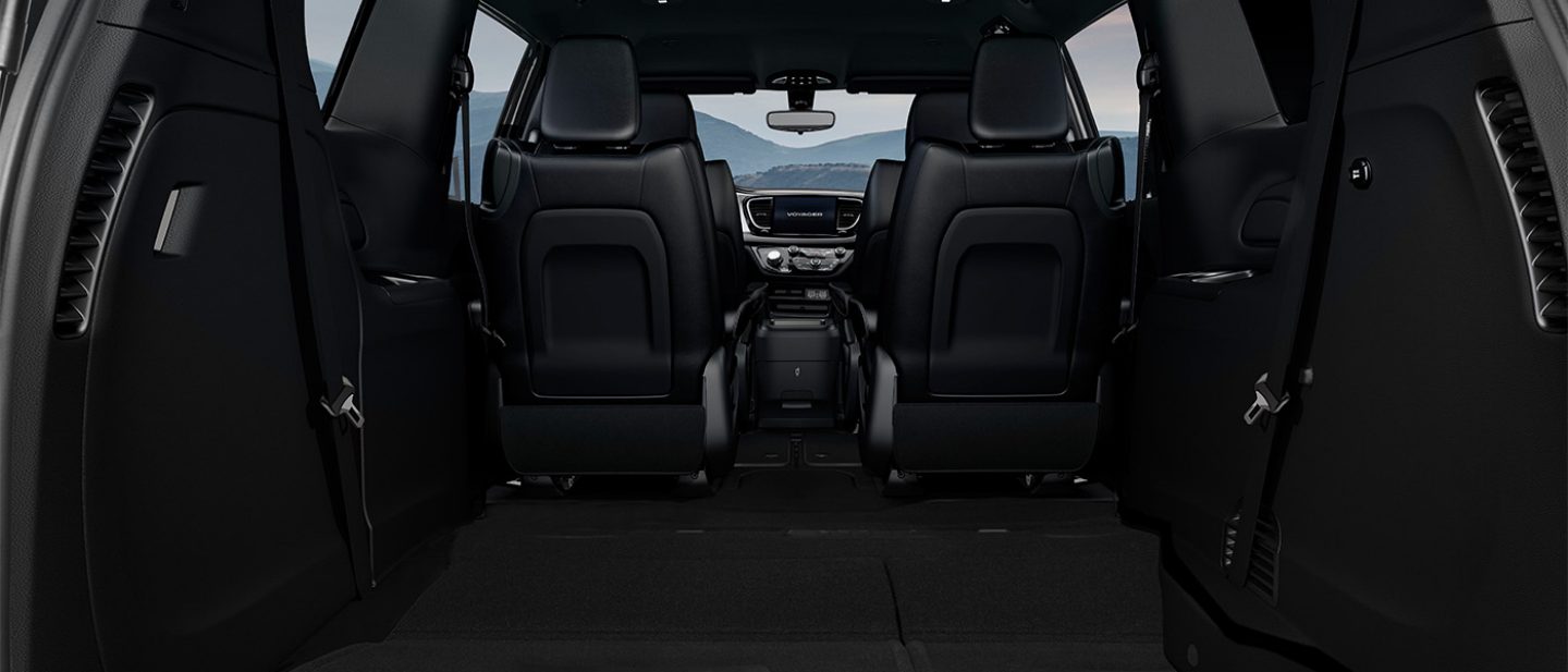 Mostrar Los asientos de la primera y segunda fila en la Chrysler Voyager LX 2025 vistos desde la parte trasera hacia el frente, con los asientos de la tercera fila plegados hacia el piso.