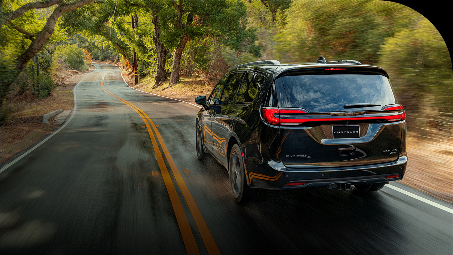 Ángulo trasero de una Chrysler Pacifica Limited AWD 2026 negra circulando por un camino rural. El fondo está borroso para indicar que el vehículo está en movimiento.