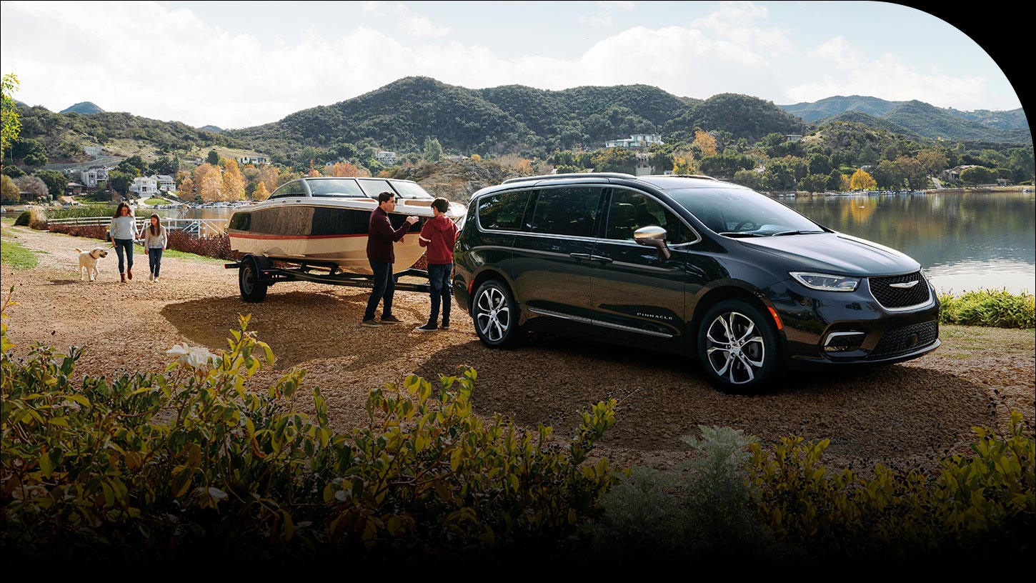 Una Chrysler Pacifica Pinnacle 2026 estacionada junto a un lago, con una lancha remolcada y una familia de cuatro miembros cerca.