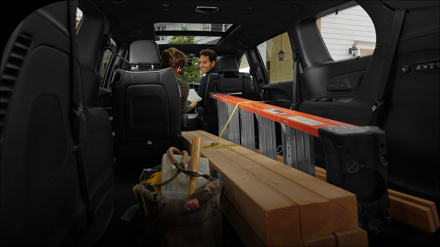 El interior de la Chrysler Pacifica 2026 con la tercera fila y uno de los asientos Stow n Go de la segunda fila plegados hacia el piso, con el fin de acomodar una escalera y piezas largas de madera.