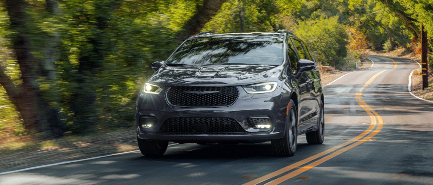 Se muestra Una Chrysler Pacifica Limited 2026 gris circulando por una carretera sinuosa en el bosque.