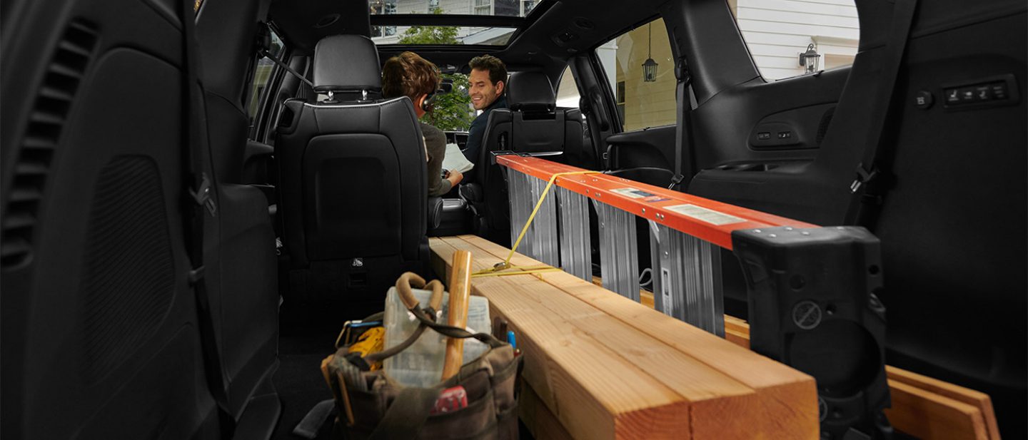 Se muestra el interior de la Chrysler Pacifica 2026 con la tercera fila y uno de los asientos Stow ’n Go de la segunda fila plegados para acomodar escalera y piezas largas de madera.