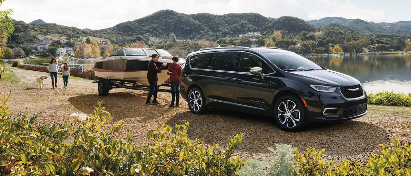 Se muestra una Chrysler Pacifica Pinnacle 2026 estacionada junto a un lago, con una lancha remolcada y una familia de cuatro miembros cerca.