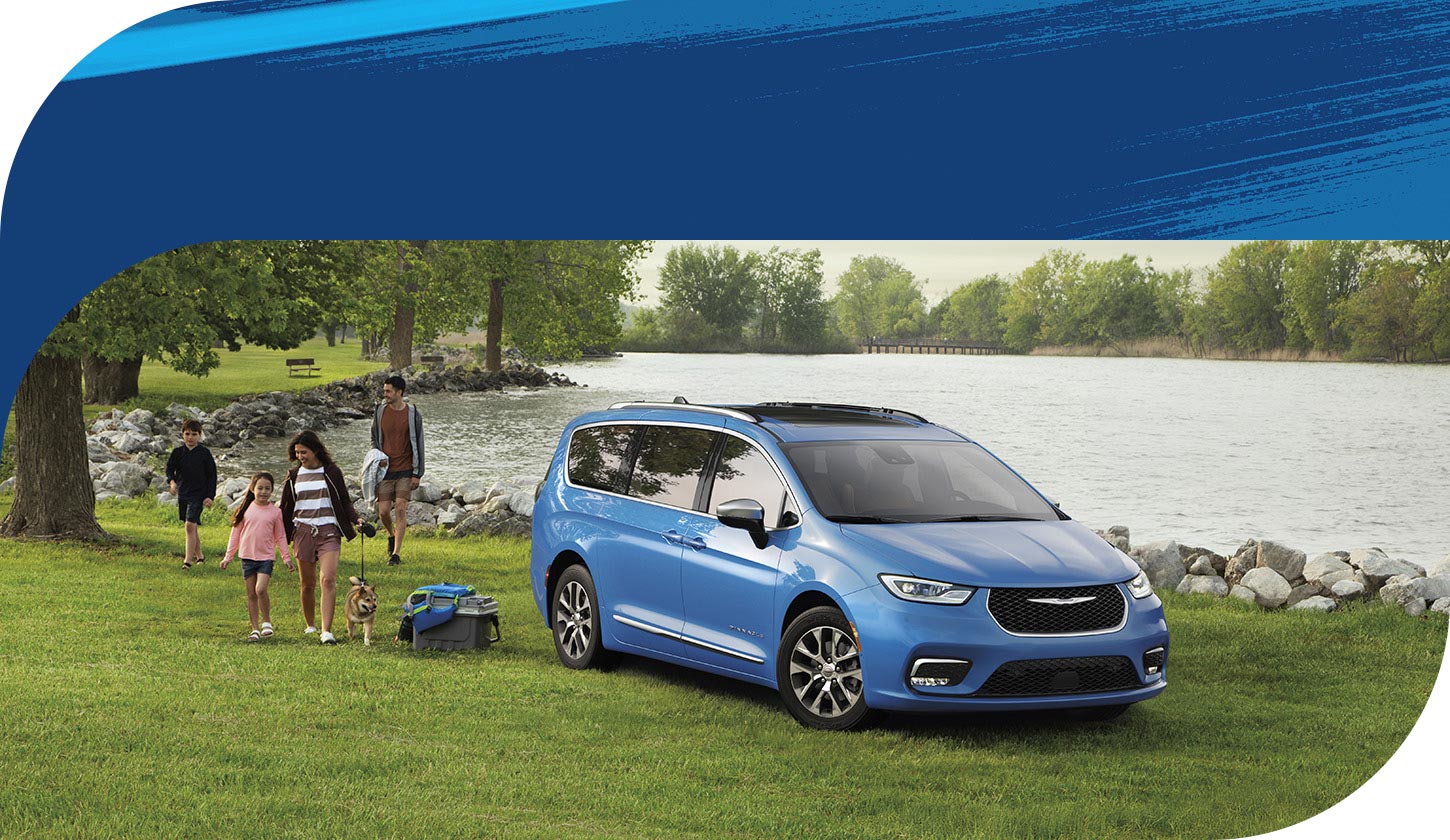 Una Chrysler Pacifica Plug-in Hybrid Pinnacle 2026 de color azul estacionada junto a un lago con una familia de cuatro personas paseando cerca.