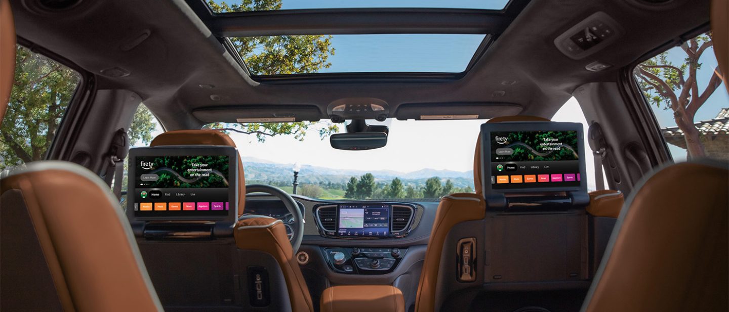 Se muestra el interior de la Chrysler Pacifica Plug-in Hybrid Pinnacle 2026, con el techo corredizo de dos paneles abierto y las dos pantallas táctiles montadas en los respaldos de los asientos de la segunda fila, todo fotografiado desde la tercera fila.