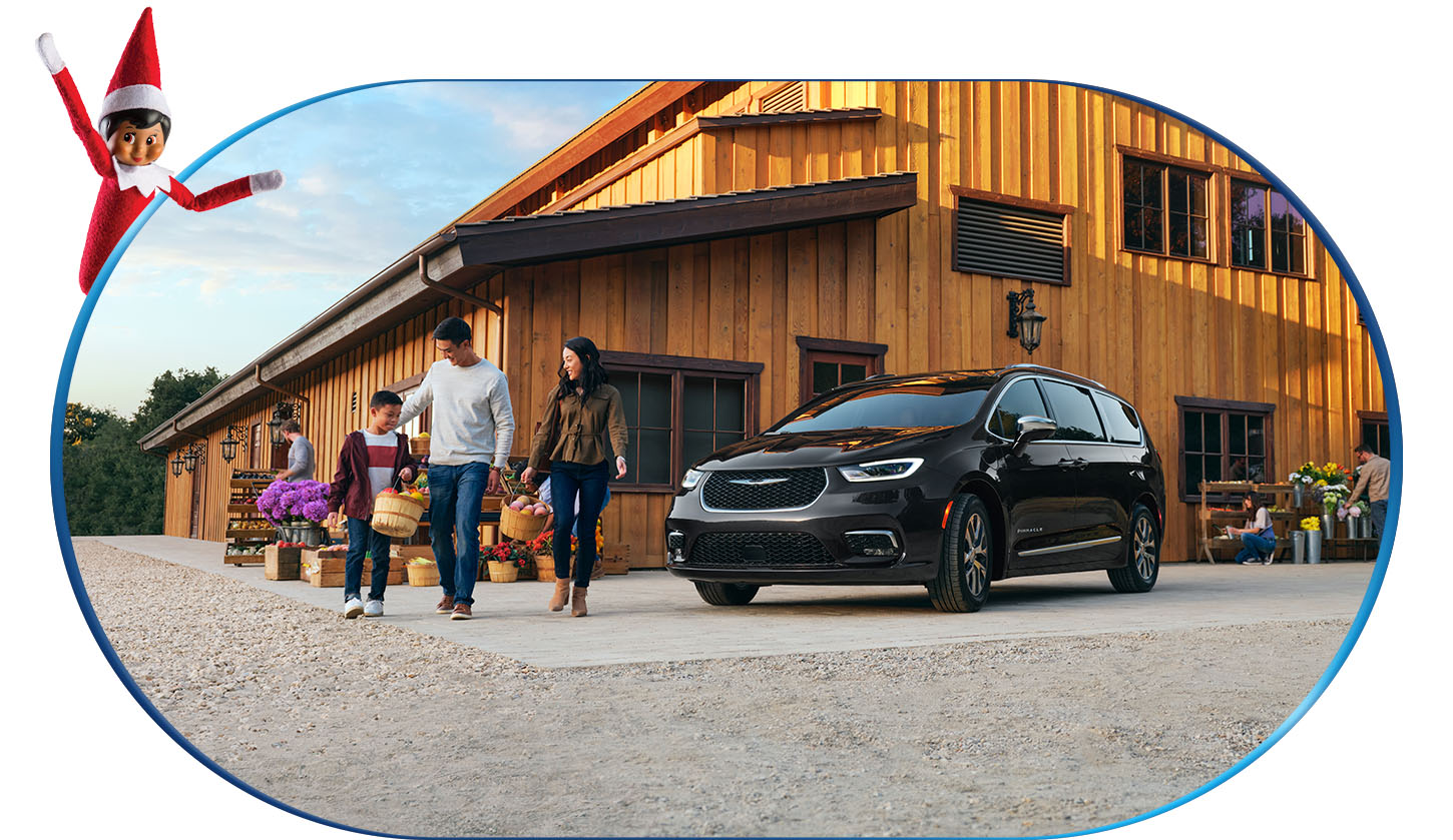 Una madre, un padre y su hijo llevando canastas de productos cerca de una Chrysler Pacifica Pinnacle Hybrid Enchufable 2026 negra en un mercado agrícola, mientras Sparkles, el duende del estante, observa desde la esquina izquierda superior de la imagen.