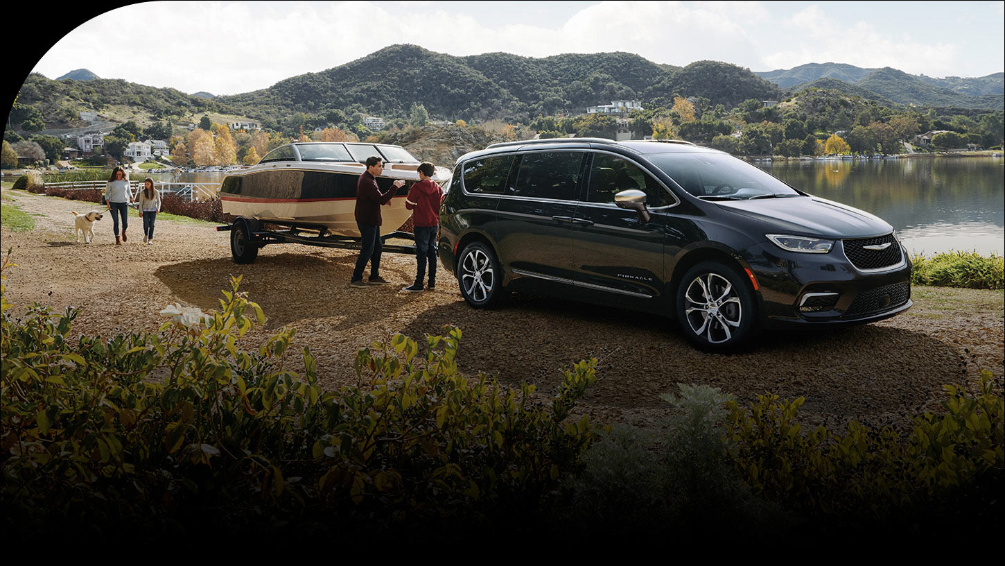 Una Chrysler Pacifica Pinnacle 2026 estacionada junto a un lago, con una lancha remolcada y una familia de cuatro miembros cerca.