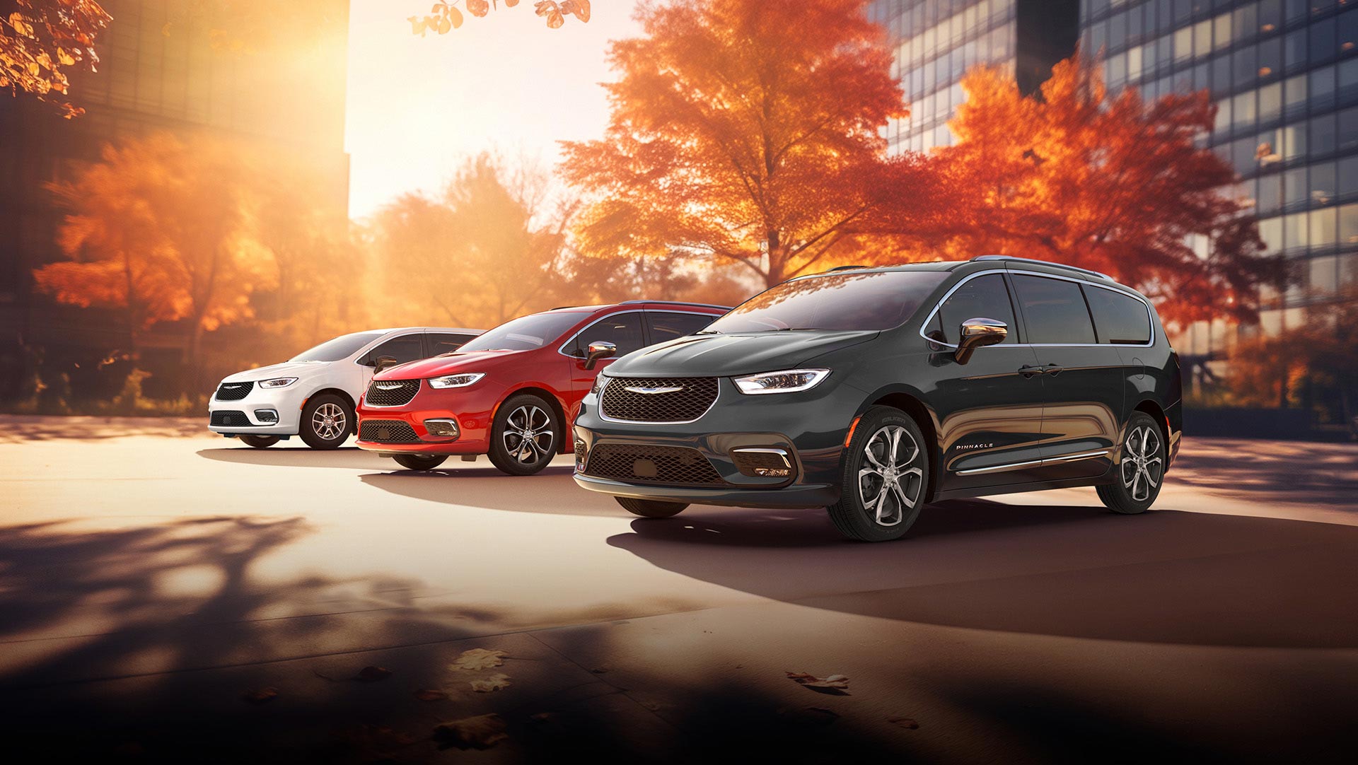 Tres modelos de la minivan Chrysler 2026 estacionados en una playa junto al mar. De izquierda a derecha: Chrysler Voyager blanca, Pacifica Pinnacle Plug-in Hybrid azul y Pacifica Pinnacle roja.