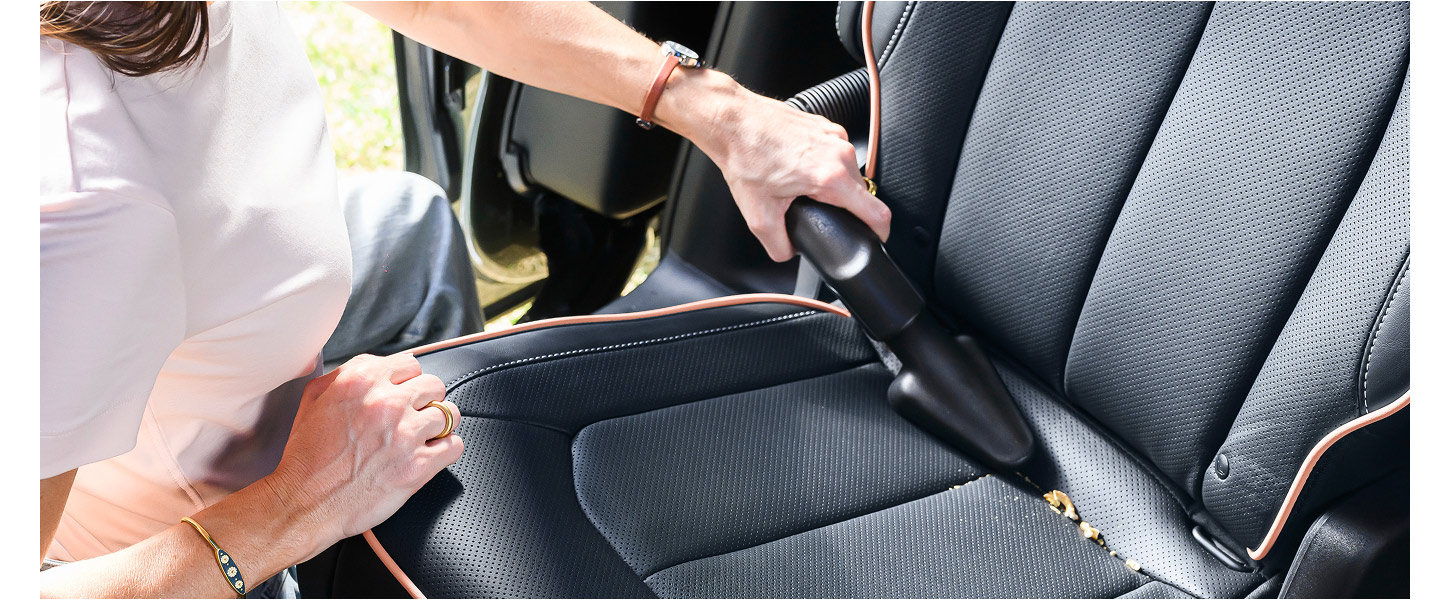 Un primer plano de una mujer de pie junto a la puerta lateral corrediza abierta de la Chrysler Pacifica 2027 pasando la aspiradora integrada sobre el alfombrado de la segunda fila.