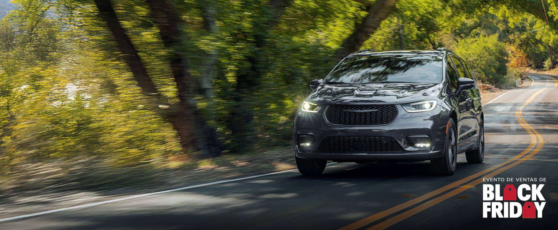 Una Chrysler Pacifica Limited 2026 gris circulando por una carretera sinuosa en el bosque. Evento de ventas Black Friday.