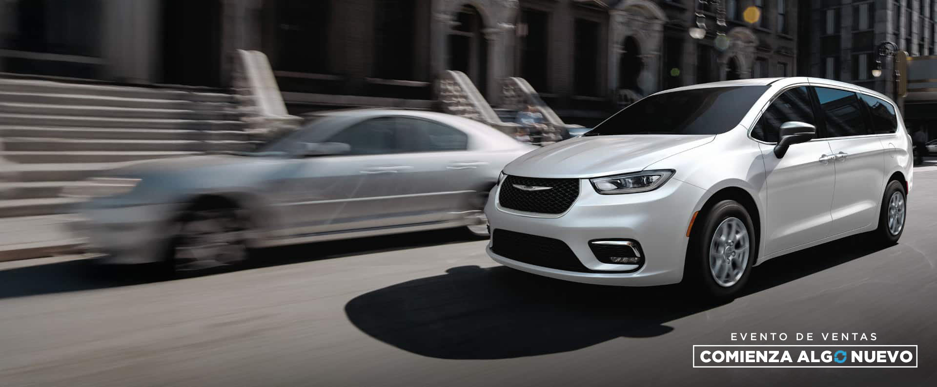 Una Chrysler Pacifica Select 2026 blanca circulando por la calle de una ciudad. Evento de ventas “Comienza algo nuevo”.