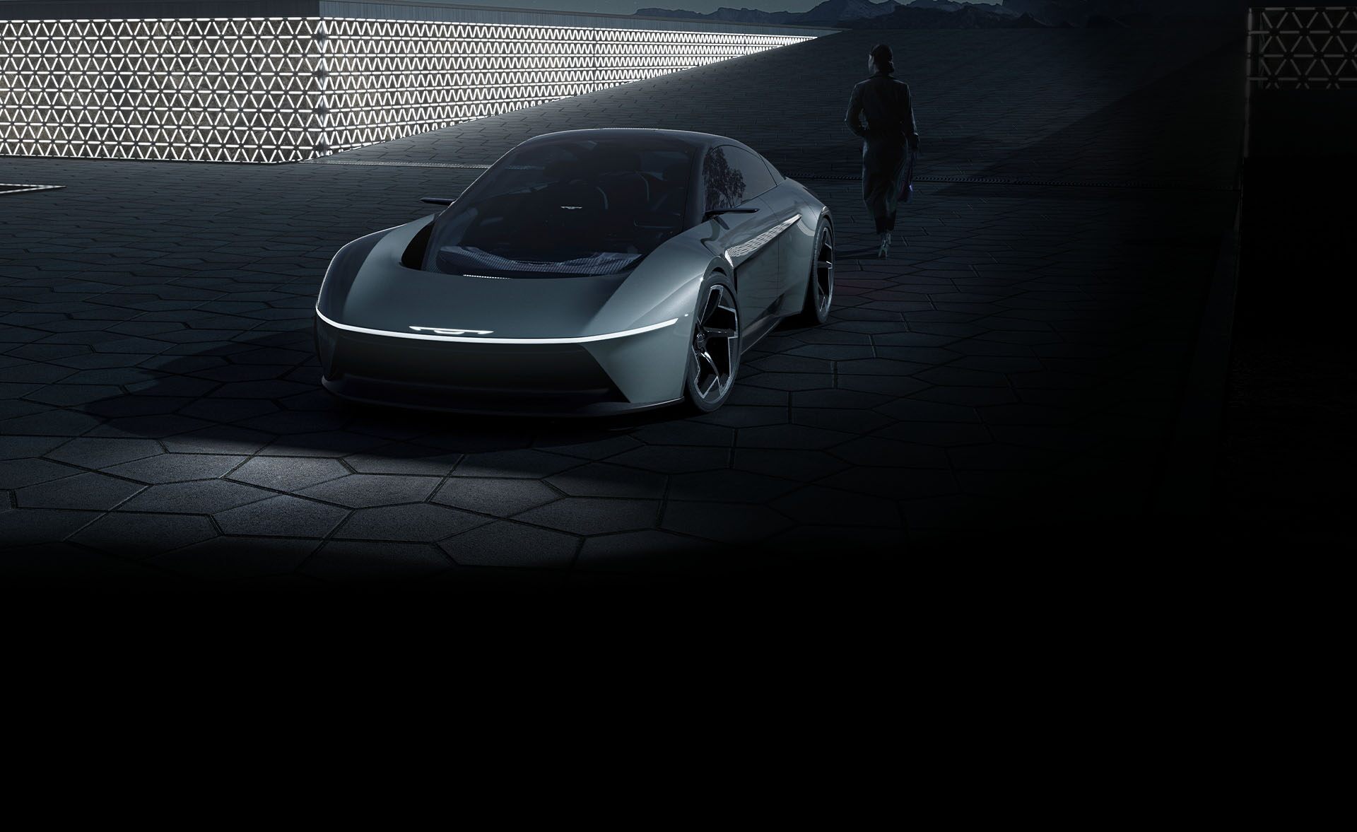 Ángulo frontal elevado de un vehículo Chrysler Halcyon Concept gris estacionado en un patio en penumbra.