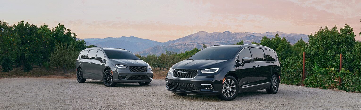 Una Chrysler Pacifica Limited 2021 y una Chrysler Pacifica Hybrid Pinnacle 2021 estacionadas en un claro en las montañas.