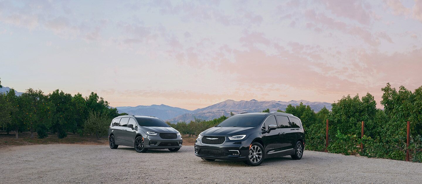 Una Chrysler Pacifica Limited 2021 y una Chrysler Pacifica Hybrid Pinnacle 2021 estacionadas en un claro en las montañas.