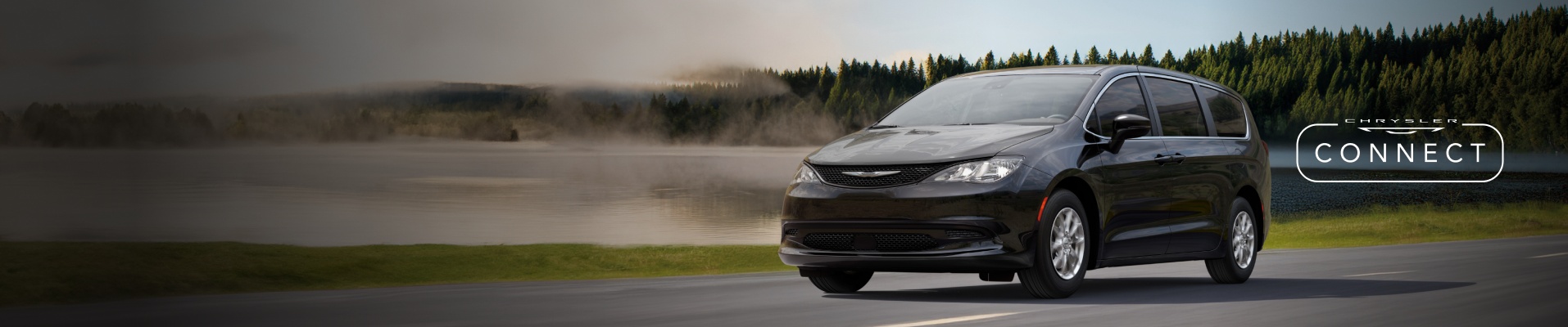 Un ángulo frontal del lado del conductor de una Chrysler Voyager 2026 negra circulando por una carretera con un bosque al fondo. El logotipo de Chrysler Connect.