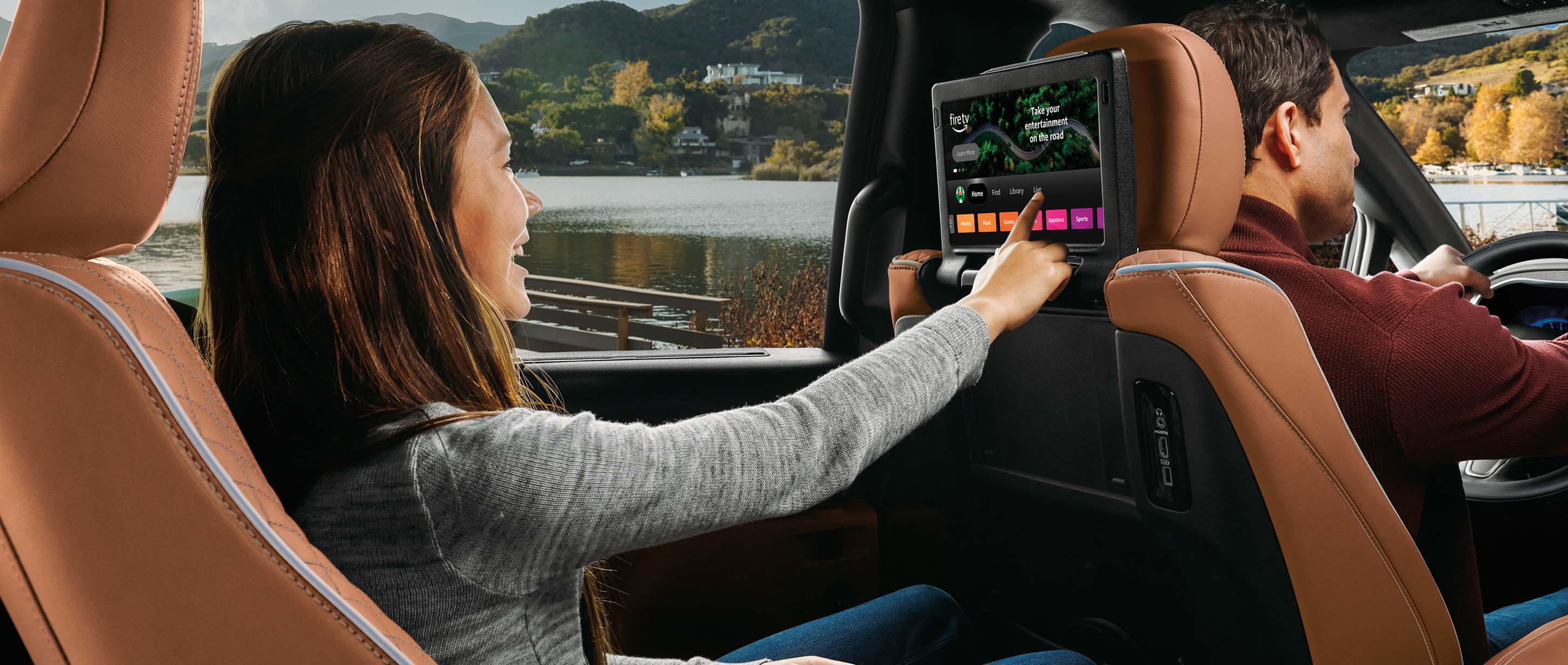 La segunda fila de la Chrysler Pacifica Pinnacle 2024, con una niña joven haciendo una selección en la página de Amazon Fire TV exhibida en la pantalla táctil montada en la parte trasera del asiento del conductor.